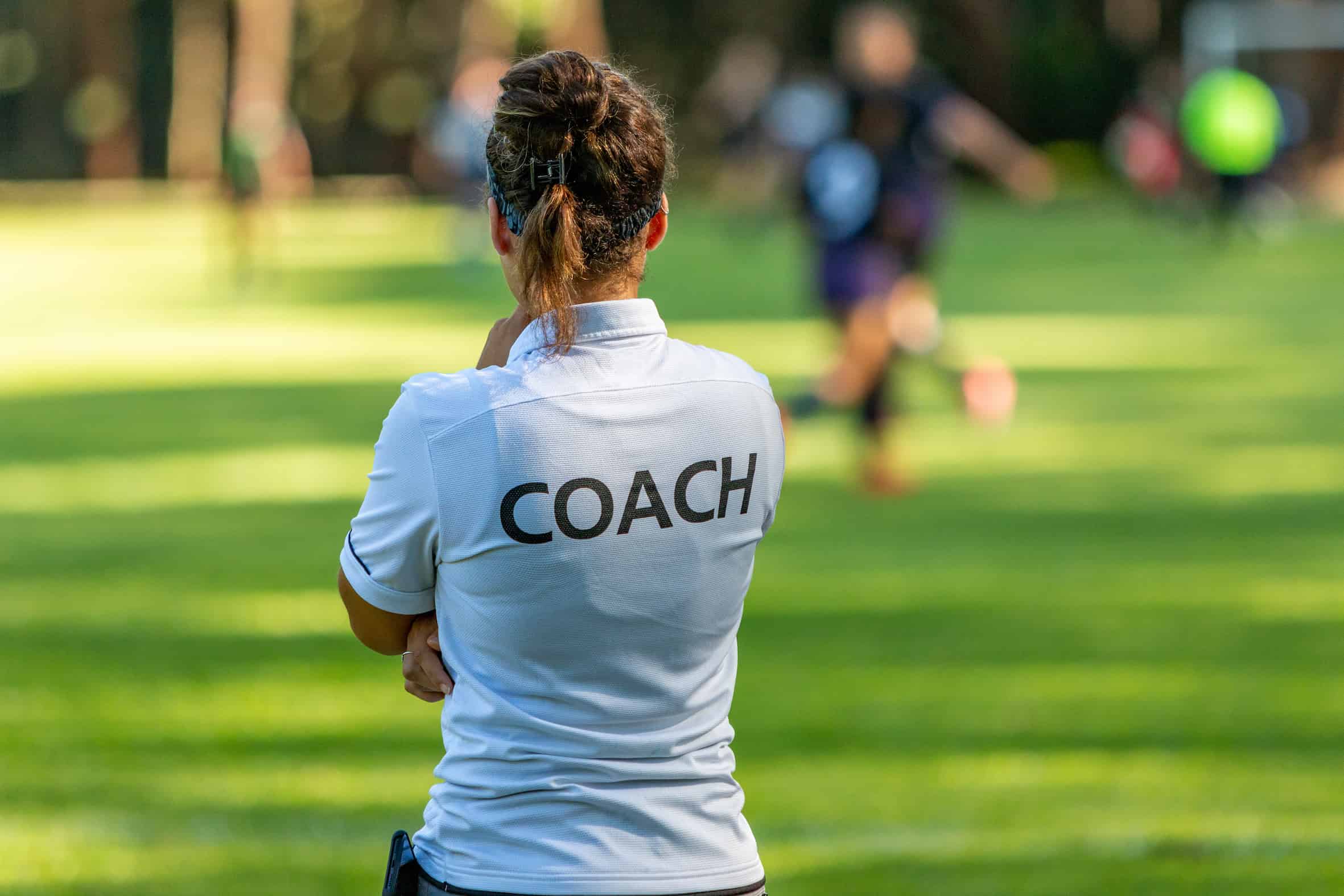 Back view of a female sport coach watching her team compete at an outdoor football field